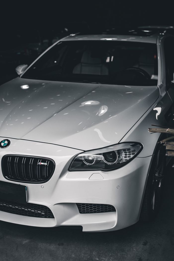 who-we-are Stylish white luxury car with BMW badge under soft lighting in a dark garage.